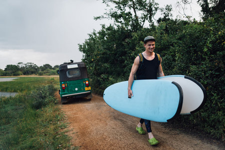 a man happily carries two surfboards from a taxi on the way