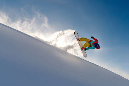 girl snowboarder jumping front flip leaving behind a wave of snowの写真素材