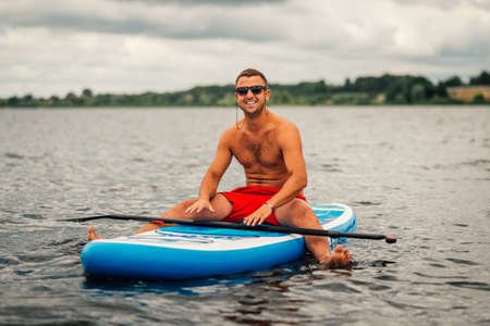 a man in shorts sitting relaxed on a sup surfの写真素材