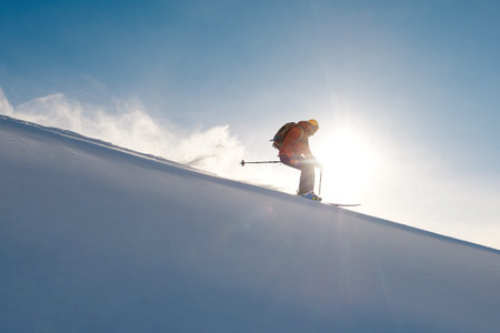 skier rides freeride on powder of snow leaving wave on sky background