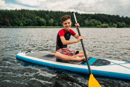 cheerful teenager sitting on a sap surf in Turkish and rowing with an oar