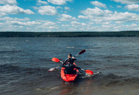 Two guys in wetsuits on a red kayak swim out into the distance on the lake, rear view.の写真素材