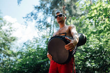 guy in glasses and red shorts playing a djembe in the woodsの写真素材