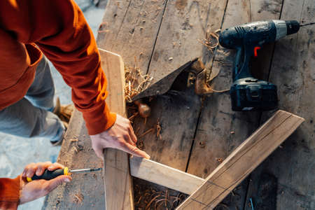 a worker fastens a wooden rail with a screw with a screwdriver, on a table in sawdustの写真素材