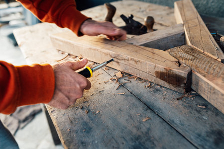 a worker fastens a wooden rail with a screw with a screwdriver, on a table in sawdust