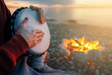 percussionist plays djembe on the seashore near the fire, hands close up