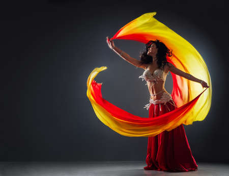 beautiful black-haired girl in a red ethnic dress on the stage dances oriental dancing waving fabric in her handsの写真素材