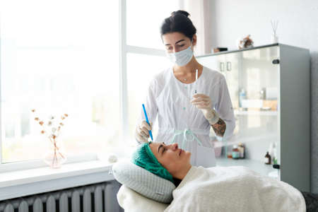 The beautician marks points for cosmetic injection on the womans face. Preparation for a cosmetic anti-aging procedure.の写真素材