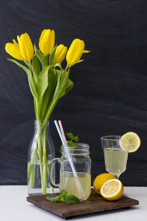 Lemonade and yellow tulips in glass bottles. On a dark backgroundの写真素材