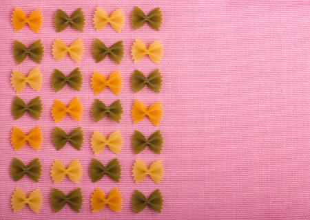 Macaroni farfalle colored. Three colors. On a pink background
