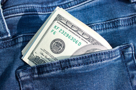 Banknotes of hundreds of US dollars sticking out of a pocket of jeans. American currency