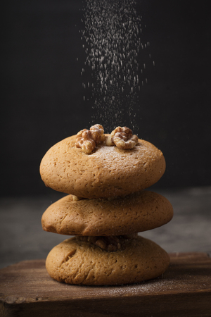 Honey cookies with walnuts on a wooden board sprinkled with powdered sugar. Dark background. homemade food 1の写真素材