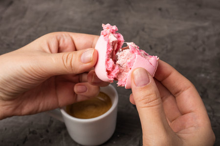 Tasty macaron is broken in half in female hands. Dark backgroundの写真素材