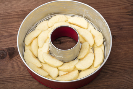 The stage of preparation of apple pie (Charlotte). Shape with apples, on a wooden backgroundの写真素材