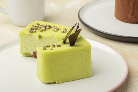 Pistachio cake on a plate, decorated with pieces of chocolate, cut in half. Light background. Close-upの写真素材