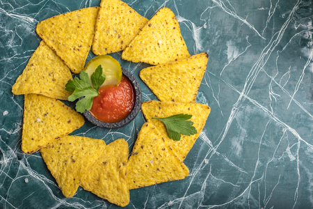Tortilla Corn Chips or Nachos with sauce in a black bowl, on a beautiful, blue background. View from above. Copy spaceの写真素材
