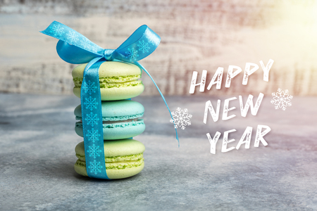 Greeting card happy new year. three macarons are tied by a blue ribbon with snowflakesの写真素材