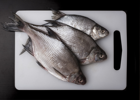 Fresh bream fish on a plastic cutting board, white. Dark background. View top. Cooking Fishの写真素材