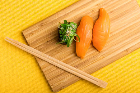 Chukka gunkan seaweed rolls and salmon sushi on a bamboo packing board. Yellow background. Top viewの写真素材