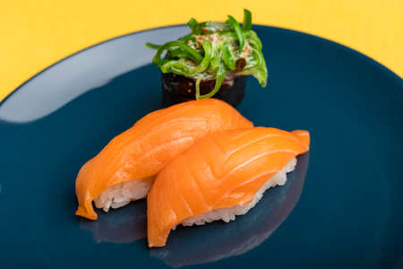 sushi with salmon and seaweed roll on a blue plate. Yellow background. Serving Japanese foodの写真素材