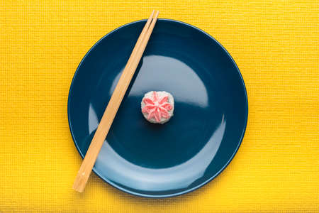 Rice sushi roll with Lava sauce lies on a blue plate with bamboo sticks. Yellow background. Minimalist style. Top viewの写真素材