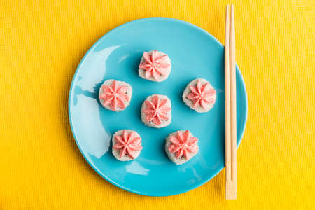 sushi roll of rice with pink Lava sauce on a blue plate with chopsticks, on a yellow background. Serving Japanese food. top viewの写真素材