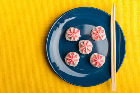 rice sushi roll with pink Lava sauce, on a dark blue plate with bamboo sticks with space for text. Yellow background. Top view, with copy spaceの写真素材