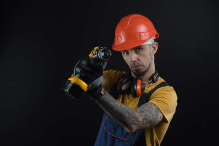 a young man posing on a black background in a work uniform and a construction toolの写真素材