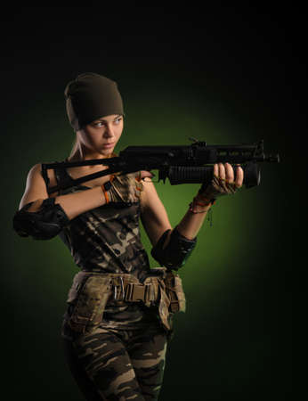 the girl in military overalls airsoft posing with a gun in his hands on a dark background in the hazeの写真素材