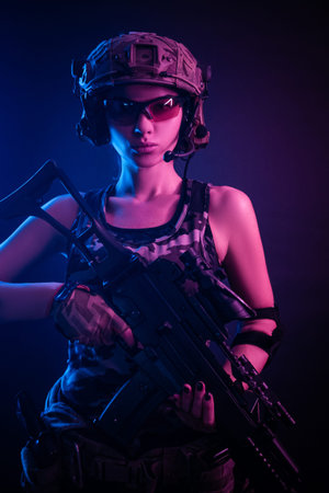 the girl in military overalls airsoft posing with a gun in his hands on a dark background in the...