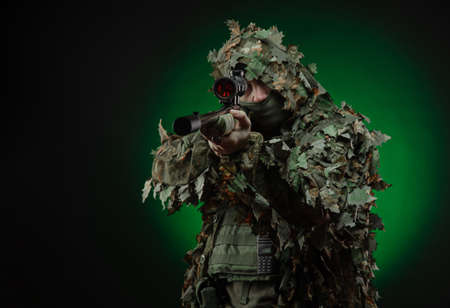 sniper in a poncho camouflage suit and a sniper rifleの写真素材
