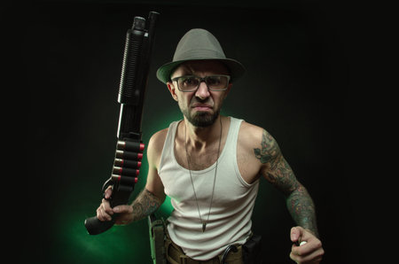 an athletic guy with a tattoo poses with a shotgun