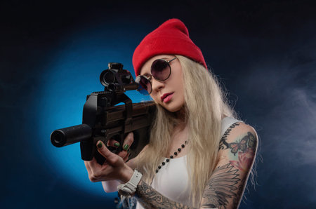 a bright blonde in a red hat with a submachine gun on a dark background