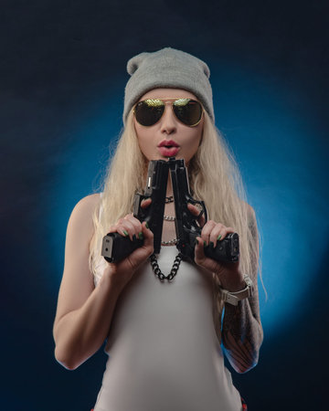 a bright blonde in a red hat with a shotgun on a dark backgroundの写真素材