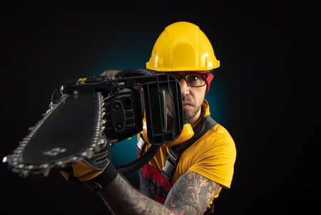 a guy in protective overalls with a chainsaw on a dark backgroundの写真素材