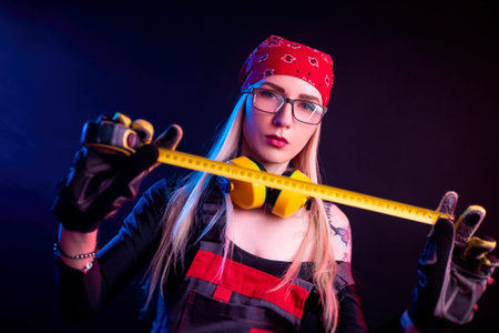 a girl in construction overalls and headphones on a black background in neon light doing house repairsの写真素材