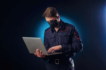 a handsome guy in a police uniform with a laptop on his face and a medical mask .の写真素材