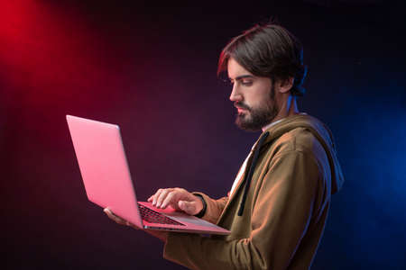 bearded guy in hoodie with laptop in neon lightの写真素材