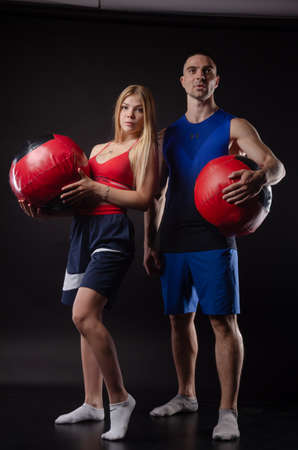 athletic man and girl stand with balls in their hands on a dark backgroundの写真素材