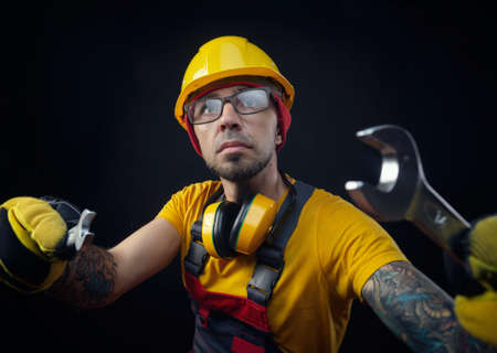 a guy in overalls and a construction helmet with a wrenchの写真素材