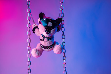 toy bear dressed in leather belts harness accessory for BDSM games on a dark background in neon...