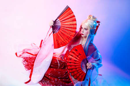 a woman in a geisha costume with fans sits on a white backgroundの写真素材