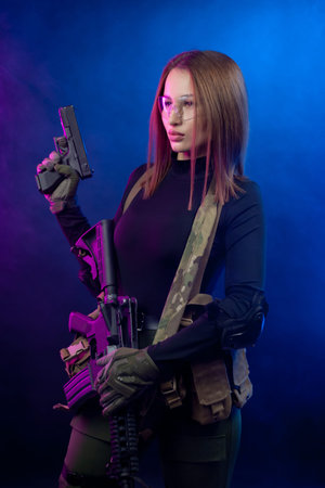 a woman in military airsoft uniform with an American automatic rifle and pistol on a dark background