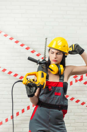 a woman in a hard hat and overalls with a puncher on the background of a white textured brick wallの写真素材