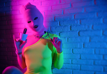 sexy woman in pink mask with cactus on white brick wall background in neon lightの写真素材
