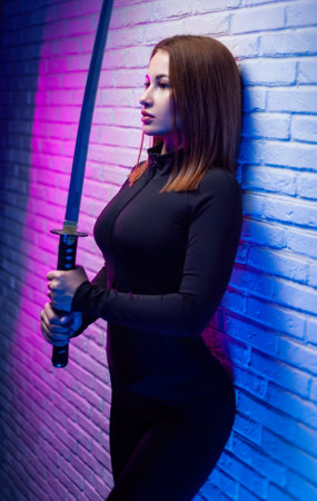 sexy slender woman in black clothes with a katana in her hand in neon lightの写真素材