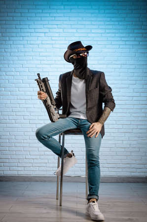 fashionable stylish man in a jacket and a cowboy hat in a balaclava with a gunの写真素材