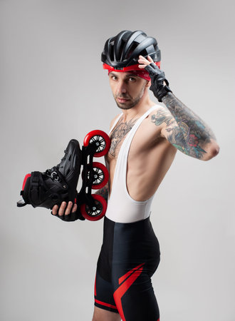 a man in sports clothes and a helmet with roller skates in his hands on a white background