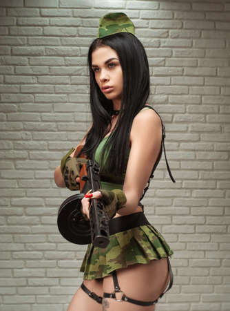 A woman in a sexy military uniform with a World War II PPSH-41 submachine gun is dressed in a short skirt and leather beltsの写真素材