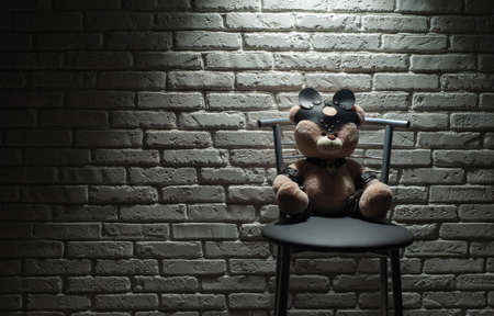 toy bear dressed in leather straps accessory for bdsm games in hard light against a brick wallの写真素材